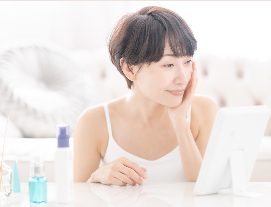 鏡を見てスキンケアする女性の画像